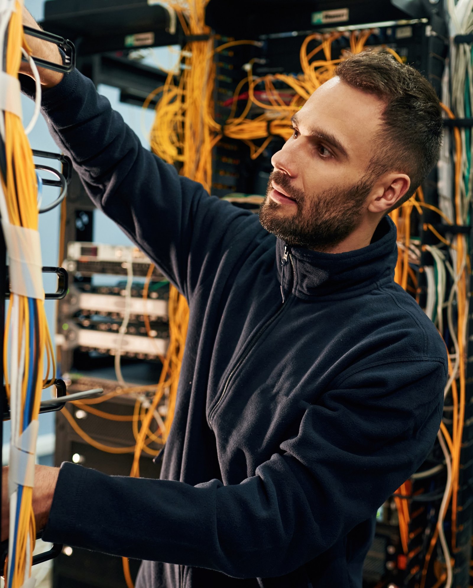 Black clothes. Young man is working with internet equipment and wires in server room